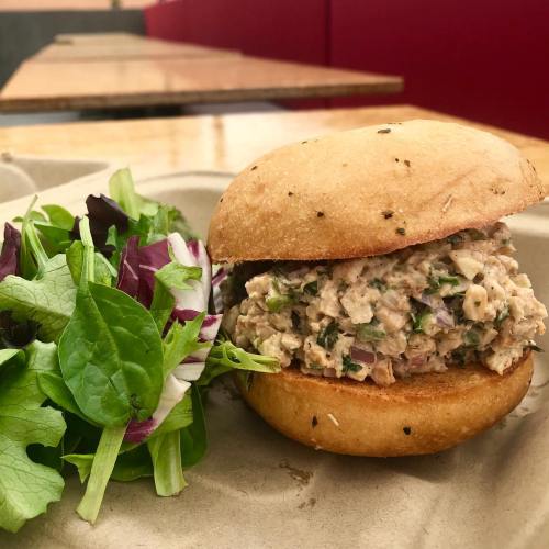 A sandwich filled with a creamy mixture, served with a side of fresh mixed greens on a paper plate.