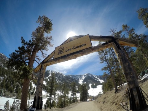 Wooden archway sign for Lee Canyon, surrounded by trees and mountains under a clear blue sky.