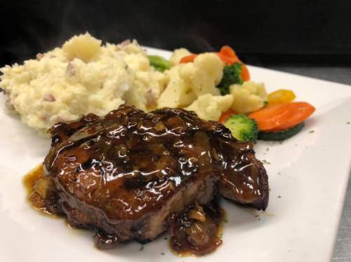 A plate featuring a glazed steak, creamy mashed potatoes, and a colorful medley of steamed vegetables.