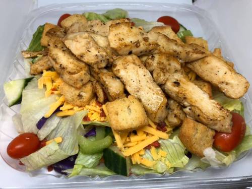 A fresh salad topped with grilled chicken, cheese, croutons, cherry tomatoes, and mixed greens in a clear container.