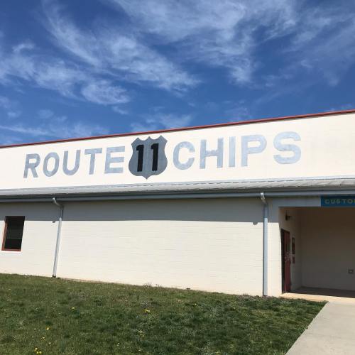 Sign on a building reading "Route 11 Chips" against a blue sky with scattered clouds.