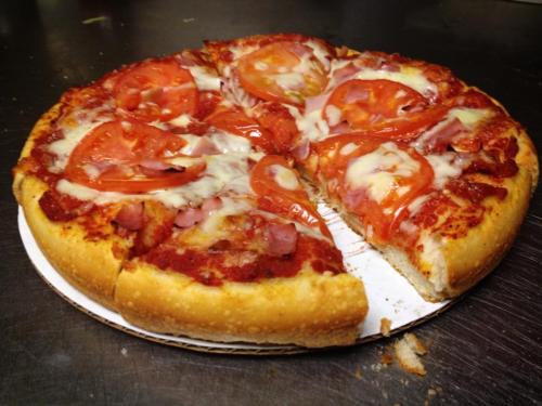 A freshly baked pizza with tomato slices, ham, and melted cheese, partially sliced on a cardboard base.