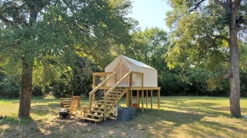 A small wooden cabin on stilts surrounded by trees, with a staircase leading up to the entrance.