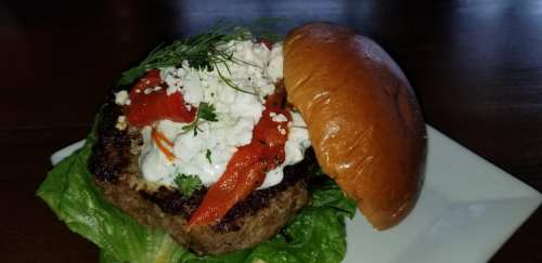 A juicy burger topped with smoked salmon, feta cheese, and fresh herbs, served on a soft bun with lettuce.