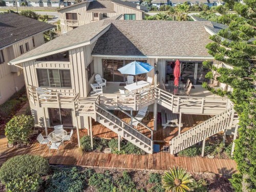 Aerial view of a two-story house with a deck, patio furniture, and surrounding greenery.
