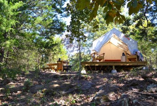 A cozy glamping tent on a wooden deck surrounded by trees, with outdoor seating nearby.