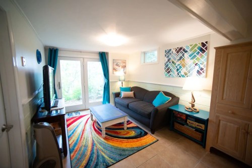 Cozy living room with a gray sofa, colorful rug, blue accents, and large windows overlooking greenery.