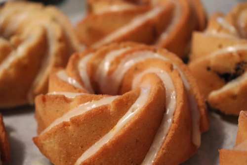 Close-up of golden-brown bundt cakes drizzled with white icing, arranged on a baking sheet.