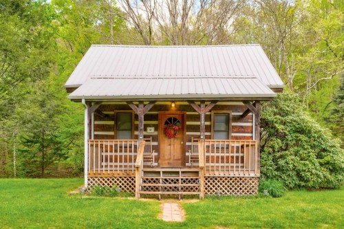 A cozy log cabin with a front porch, surrounded by greenery and a wreath on the door.