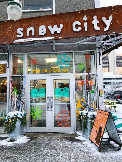 Exterior of Snow City café with colorful snowflake decorations and a welcoming entrance, surrounded by winter scenery.