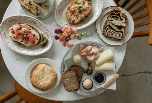 A table with various dishes, including bread, spreads, pickles, and pastries, surrounded by flowers.