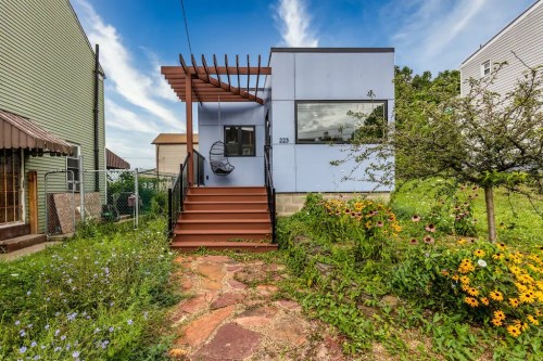 A modern house with a wooden deck, surrounded by colorful flowers and greenery under a blue sky.