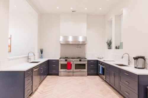 Modern kitchen with navy blue cabinets, stainless steel appliances, and a herringbone wood floor. Bright and spacious design.