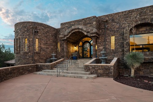 A grand stone entrance with arched doorways, steps, and decorative lighting against a cloudy sky.