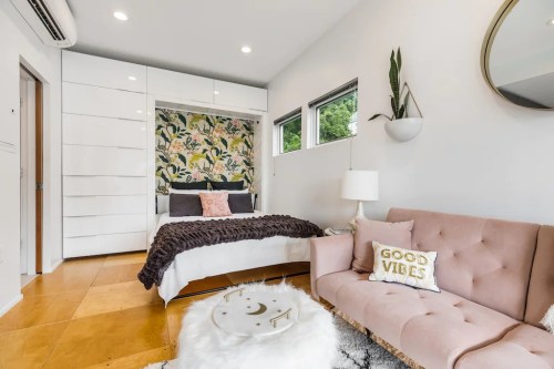 Cozy bedroom with a floral accent wall, a pink sofa, and modern decor, featuring a bed and stylish accessories.