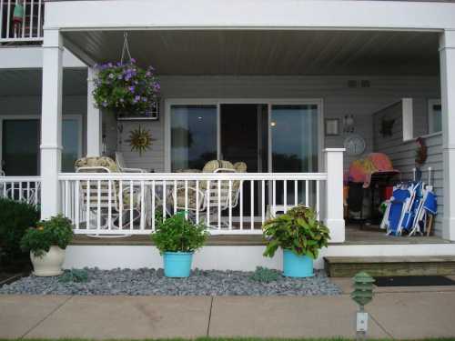 A cozy porch with wicker chairs, potted plants, and a hanging flower basket, overlooking a peaceful outdoor area.