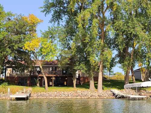 A serene lakeside view featuring a house surrounded by trees and a dock with boats.