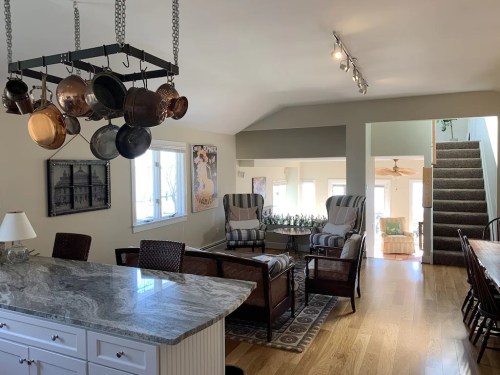A bright, open kitchen and living area with a marble countertop, seating, and a staircase in the background.