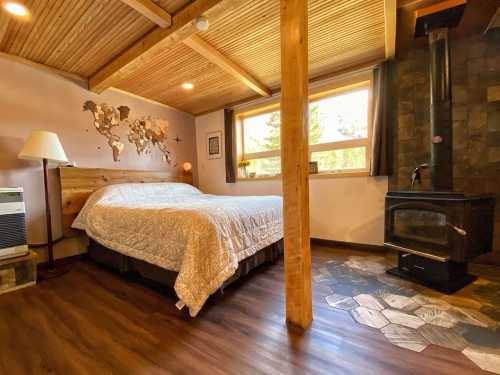 Cozy bedroom with a wooden bed, map decor, and a wood stove, featuring large windows and warm lighting.