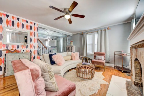 Cozy living room with colorful wallpaper, a fan, plush seating, and a decorative fireplace. Warm and inviting atmosphere.