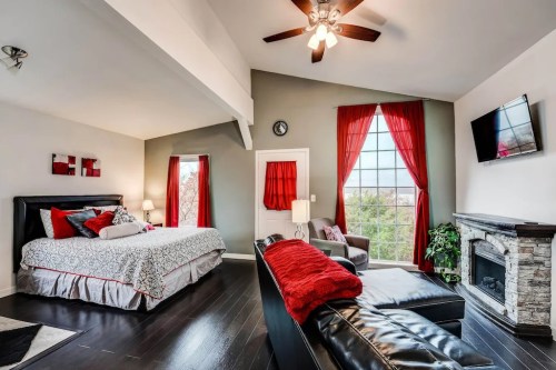 Cozy bedroom with a king bed, red accents, a fireplace, and large windows letting in natural light.