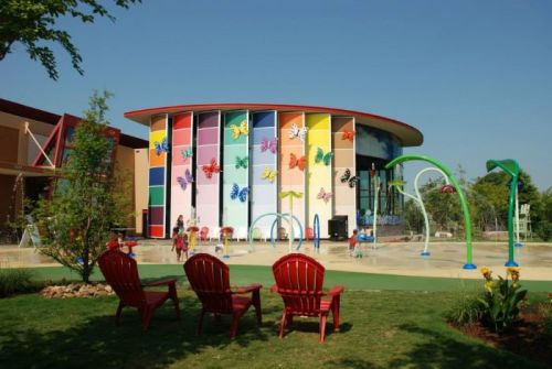 Colorful building with butterfly murals, surrounded by green grass, playground equipment, and red chairs in the foreground.