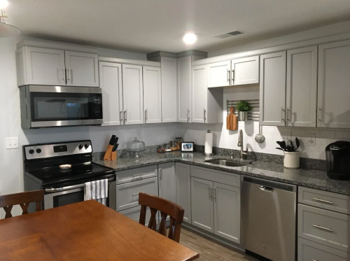 Modern kitchen with gray cabinets, stainless steel appliances, and a wooden dining table. Bright and inviting atmosphere.