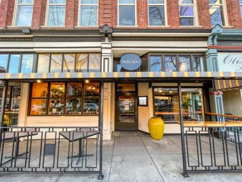 Exterior view of Mercado restaurant, featuring large windows, a striped awning, and a decorative yellow vase.