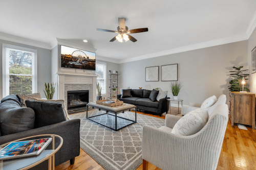 Cozy living room with a fireplace, gray sofas, a coffee table, and decorative plants, featuring a TV on the wall.