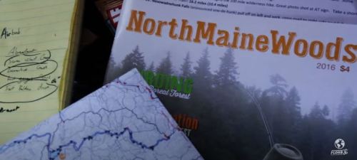 A close-up of a magazine titled "North Maine Woods" alongside a map and handwritten notes on a notepad.