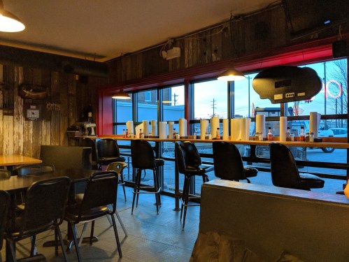 Interior of a rustic diner with empty chairs, a long counter, and condiments lined up on the window ledge.