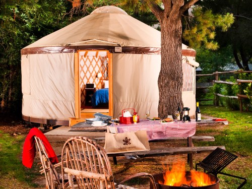 A cozy yurt with a fire pit and picnic table, surrounded by trees, creating a warm outdoor camping atmosphere.