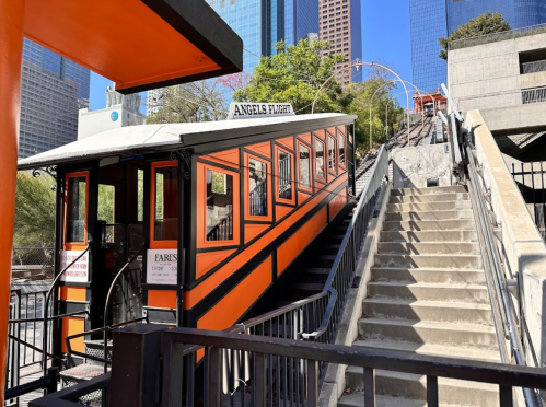A colorful funicular station with stairs beside it, set against a backdrop of tall buildings in a city.