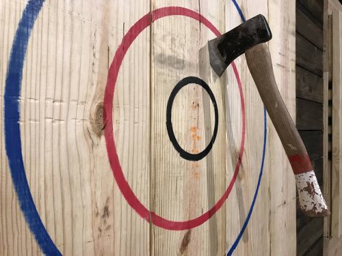 An axe embedded in a wooden target with concentric colored circles.