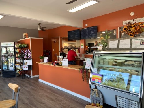 Interior of a cozy café with an orange accent wall, display cases, and a counter where staff are preparing food.