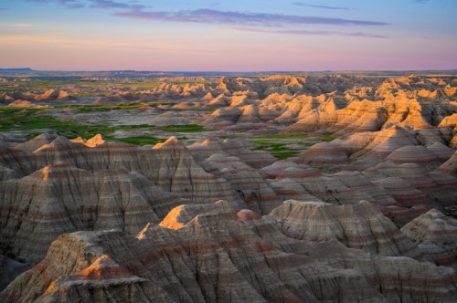 A panoramic view of rugged, colorful rock formations at sunset, with green valleys in the background.