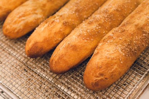 Freshly baked breadsticks with a golden crust and sprinkled salt, resting on a wire cooling rack.