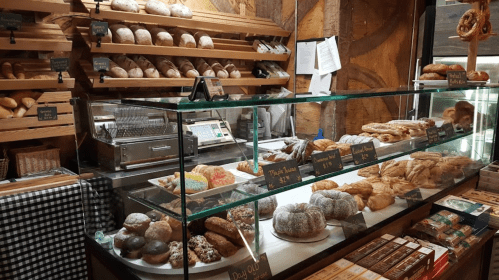 A bakery display featuring various breads, pastries, and desserts in a rustic setting with wooden shelves.