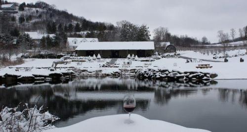 A snowy landscape featuring a rustic building by a pond, with a glass of red wine in the foreground.
