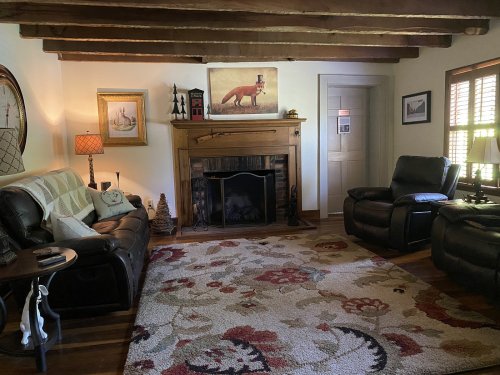 Cozy living room with wooden beams, a fireplace, plush seating, and a colorful area rug. Warm and inviting atmosphere.