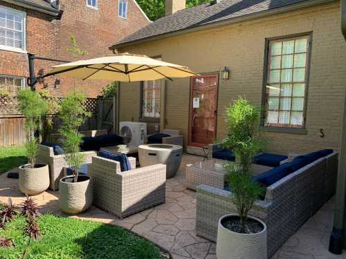 A cozy outdoor patio with wicker furniture, an umbrella, and potted plants, set against a brick house backdrop.