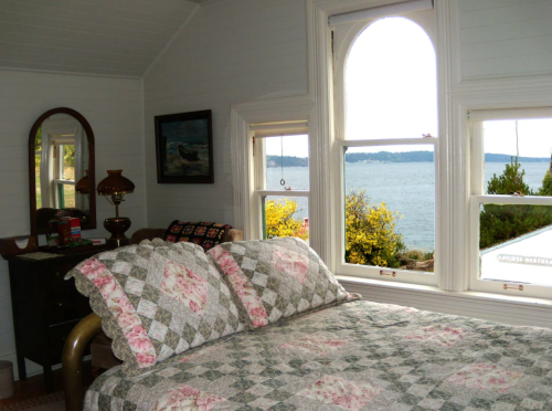 Cozy bedroom with a quilted bed, vintage decor, and a view of the water through large windows.