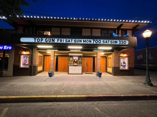 A movie theater at night with a marquee displaying showtimes for "Top Gun" and a welcoming entrance.
