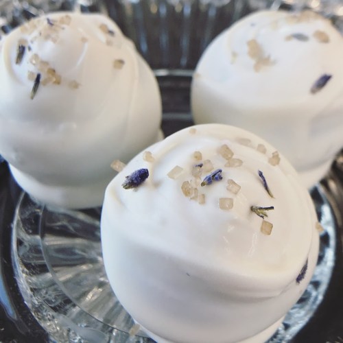 Three white dessert balls topped with lavender and sugar crystals, arranged on a clear plate.