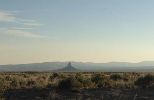 A distant rock formation rises above a vast, open landscape under a clear sky.