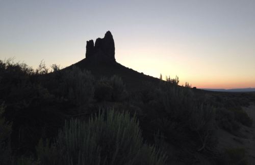 Silhouette of a rocky formation against a sunset sky, surrounded by sparse vegetation.