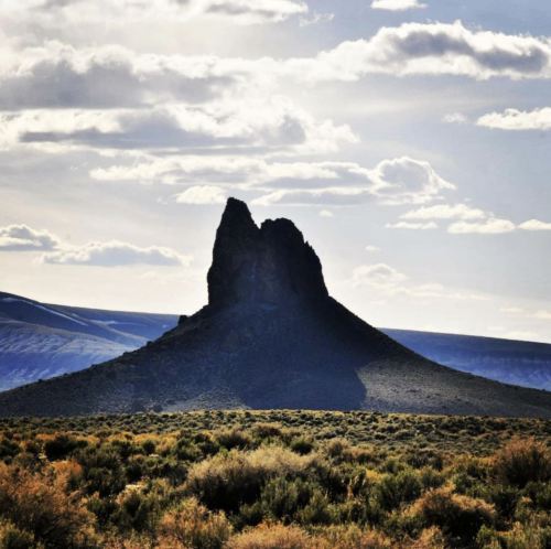 A solitary rock formation rises from a grassy landscape under a cloudy sky.