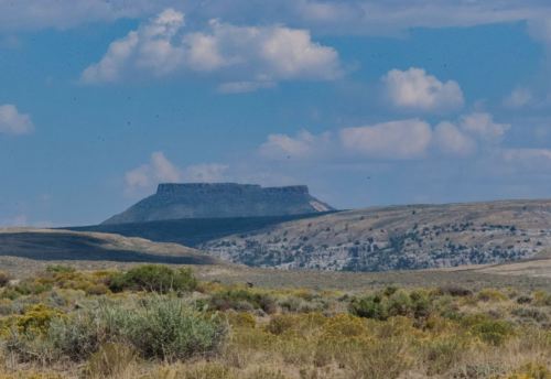 A distant plateau rises above a grassy landscape under a blue sky with scattered clouds.
