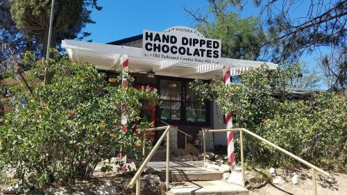 A charming shop with a sign reading "Hand Dipped Chocolates" surrounded by greenery and a clear blue sky.