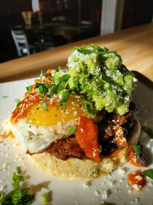 A delicious breakfast dish featuring a fried egg, avocado, salsa, and herbs on a biscuit.